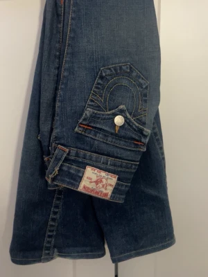 True Religion blå jeans med fickdetaljer - True religion jeans köpta från Tokyo nån gång i 2000 talet dom är väldigt lågmidjade och är bootcut              Dragkedjan har gått sönder men det går att fixa om man fixar en ny dragkedja eller syr ihop den annars är jeansen perfekta