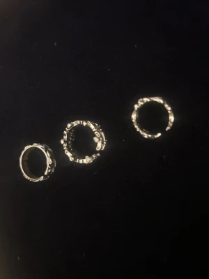 Tre silvriga ringar med unik struktur - Säljer tre silvriga ringar med cool, oregelbunden och nästan organiskt formad yta. Ringarna har en rå och trendig design med detaljer som påminner om små blommor eller snirkliga mönster. Perfekta för dig som gillar att sticka ut med dina accessoarer.