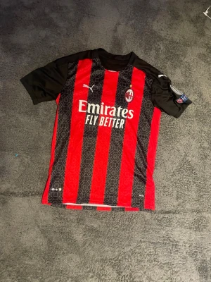 AC Milan matchtröja Ibrahimovic #21 - Säljer en AC Milan matchtröja med Ibrahimovic och nummer 21 på ryggen. Tröjan är röd och svart med vertikala ränder, korta svarta ärmar och klubbmärke på bröstet. Materialet är lätt och andas, perfekt för fotbollsträning eller support. Passar som M