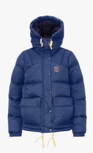 Blå pufferjacka från Fjällräven - Blå pufferjacka från Fjällräven med huva, gula dragskor och två stora fickor framtill. Jackan har en klassisk pufferdesign med broderad logotyp på bröstet och tryckknappar. Perfekt för kalla vinterdagar.