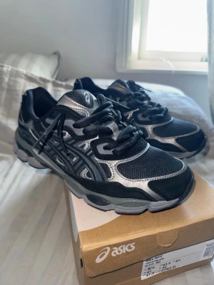ASICS GEL-NYC svarta sneakers - Svarta och grå ASICS GEL-NYC sneakers med coola detaljer och meshpaneler för extra andningsförmåga. Snygg sportig look med klassisk ASICS-logga på sidan och robust sula. Perfekta för dig som gillar streetstyle och bekväma skor.