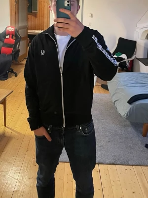 Svart full zip från Fred Perry - Säljer en svart Fred Perry full zip i storlek M. Den är i gott skick, men har en liten defekt på undersidan av armen (se bild 2) Hör av er vid frågor!❤️‍🩹