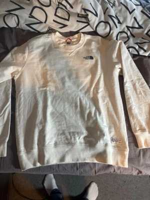 Vit sweatshirt från The North Face - Säljer en stilren vit sweatshirt från The North Face med rund halsringning och diskret logga på bröstet. Tröjan har ribbade muddar vid ärmslut och nederkant, perfekt för en avslappnad look. Materialet är mjukt och bekvämt.