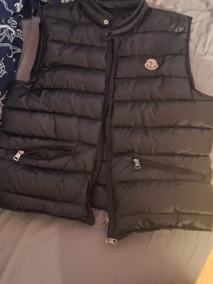 Svart dunväst från Moncler - Säljer en svart äkta dunväst från Moncler. Helt nytt skick då den ej passade mig. Västen har en glansig finish och är perfekt för lager-på-lager under kyliga dagar. Snygg och tidlös modell som funkar till det mesta. 