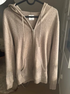 Beige hoodie i kashmir från COS - Säljer denna Zip up då den inte kommer till användning. Finns en liten defekt som visas på bilderna. Defekten är mera vid ryggen ingen tydlig defekt. Pris går att diskuteras