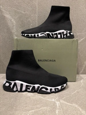 Speed Trainer svarta sneakers - Svarta Speed Trainer sneakers med stickad ovandel i textil och chunky vit sula med svart grafiskt mönster. Strumpliknande passform som sitter tight runt foten och ger en futuristisk vibe. Perfekta för dig som gillar streetstyle och vill sticka ut.