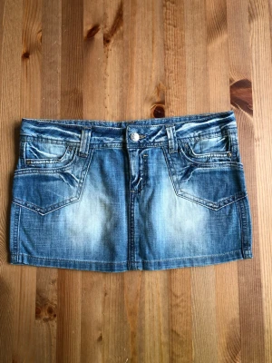 Blå jeanskjol med fickor - Snygg blå jeanskjol i kort modell med slitningar och klassiska fickor fram och bak. Kjolen har bälteshällor och knappstängning framtill. Perfekt för dig som gillar en avslappnad och trendig stil.