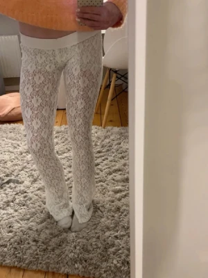 Vita spetsbyxor  - Säljer ett par vita leggings med vida ben och bred resår i midjan. Byxorna är genomskinliga och har ett snyggt blommigt spetsmönster. 