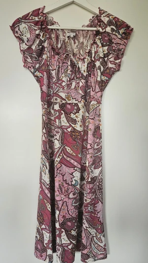 Blommig långklänning i rosa toner - Långklänning med blommigt mönster i rosa, vitt och brunt. Perfekt för varma dagar med sitt lätta material och romantiska look. (Polyester) använd endast 2 gång.