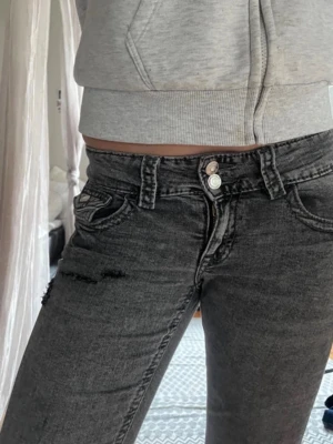 Grå slitna jeans med dubbelknäppning - Säljer ett par grå jeans med lätt slitning och dubbelknäppning fram. Jeansen har fem fickor, smal passform och raka ben. Snygg tvättad look och detaljer vid fickorna. Perfekta till en avslappnad streetstil.