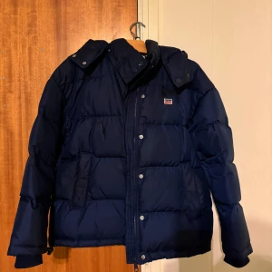 Mörkblå vinterjacka från Levis  - Säljer en mörkblå vinterjacka från Levis med huva och dragkedja. Jackan har en klassisk pufferdesign och är perfekt för kyliga dagar. Den har långa ärmar och en diskret logga på bröstet. Finns en liten fläck i framsidan också:)