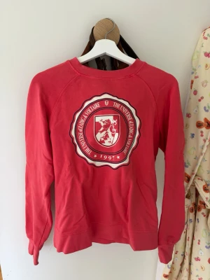 Röd sweatshirt från Zadig & Voltaire - Cool röd sweatshirt från Zadig & Voltaire med tryckt universitetsinspirerat emblem framtill och årtalet 1997. Tröjan har rund halsringning, långa ärmar och mjukt bomullsmaterial. Perfekt för en avslappnad och trendig look.