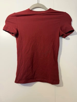 Mörkröd t-shirt från Divided XS - En enkel och snygg mörkröd t-shirt från Divided i storlek XS. T-shirten har klassisk passform med korta ärmar och rund halsringning. Materialet är mjuk bomull som känns skönt mot huden. Perfekt för dig som gillar stilrena basics.