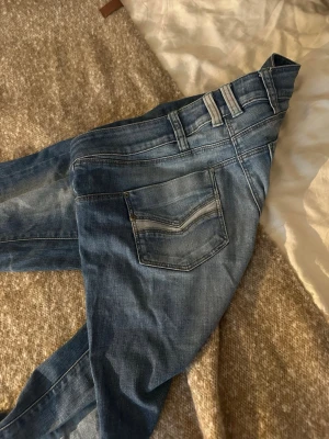 Blå jeans från Vero Moda - Säljer ett par klassiska blå jeans från Vero Moda med låg midja och bootcut ben. Jeansen har fem fickor, bälteshällor och dragkedja med knapp. Snygg tvättad lite retro look och passar perfekt till vardagsstilen eller festligheter🥰