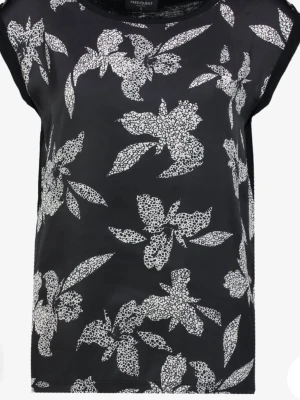 Svart blommig topp från Freequent - Snygg svart topp från Freequent med vita blommiga mönster. Toppen har rund halsringning och är ärmlös med en rak passform. Perfekt att styla med jeans eller kjol för en trendig look.