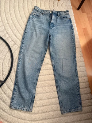 Blå raka jeans från Zara - Säljer ett par klassiska blå raka jeans från Zara i storlek 38. Jeansen har hög midja, fem fickor och stängs med dragkedja och knapp. Tillverkade i ett slitstarkt denimtyg som ger en tidlös look. Perfekta till sneakers eller boots.