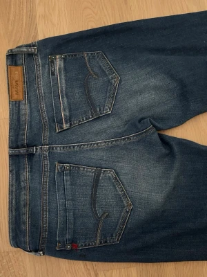 Blå raka jeans från Mavi - Säljer ett par klassiska blå jeans från Mavi med raka ben och snygga slitningar framtill. Jeansen har fem fickor, normal midja och är gjorda i mjuk denim. Perfekta för en avslappnad och trendig look.