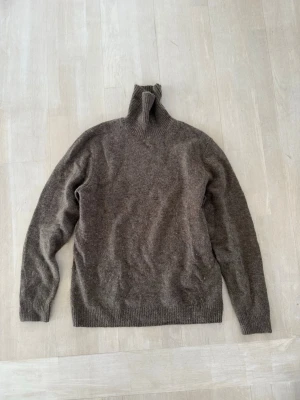 Brun polotröja i ullmix - Mysig brun stickad polotröja med lång ärm och ribbade muddar. Tröjan har en hög polokrage och är tillverkad i en mjuk ullblandning som passar perfekt för kyliga dagar. Enkel och stilren design som är lätt att matcha.