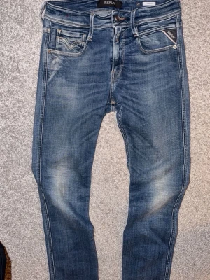 Replay Anbass blå jeans slim fit - Säljer ett par blå Replay Anbass jeans med slim fit och klassisk femficksdesign. Jeansen har snygga slitningar, dragkedja i gylfen och Replay-logga på fickan. Perfekta för dig som gillar en modern och stilren look. STORLEK WAIST 29,  LENGHT 34
