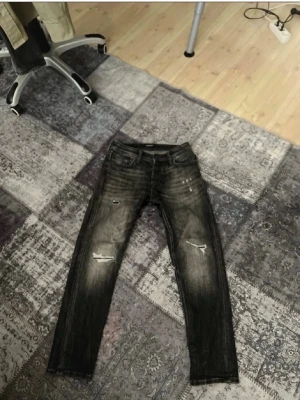 Svarta slitna jeans med slitningar - Säljer ett par svarta jeans med coola slitningar på knäna och lätt tvättad look. Jeansen har fem fickor och raka ben. Perfekta för dig som gillar en avslappnad och trendig stil. W29L32