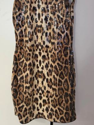 Leopardmönstrad kort klänning - Säljer en snygg kort klänning med leopardmönster. Klänningen är ärmlös, har öppen rygg och en tight passform. Materialet känns stretchigt och bekvämt och är endast använd 1 gång i storlek S