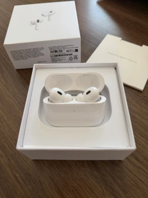 Apple AirPods Pro med laddningsetui - Säljer ett par vita Apple AirPods Pro med trådlöst laddningsetui. Hörlurarna har en stilren och kompakt design i plast och levereras med originalförpackning, laddningskabel och extra öronproppar. Perfekta för dig som vill ha grymt ljud och brusreducering.