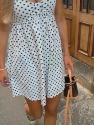 Trendig Vit prickig sommarklänning från Zara  - Söt vit kortklänning med svarta prickar och smala axelband. Klänningen har en lätt utställd passform och markerad midja, perfekt för varma dagar. Tillverkad i ett mjukt och luftigt material som känns skönt mot huden.