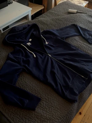 Marinblå hoodie från Levi's - Säljer en marinblå hoodie från Levi's med dragkedja framtill och vita dragsnören i huvan. Klassisk passform med två fickor framtill och liten röd Levi's-logga på bröstet. Perfekt för dig som gillar en enkel och stilren look. Inga som helst defekter eller märken/fläckar! Som ny! Storlek M herr😌