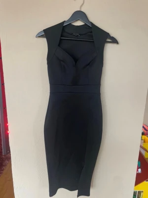Svart figurnära klänning med slits XS - Säljer en svart, figurnära klänning med breda axelband och snygg v-ringning. Klänningen har en liten slits framtill och är knälång, vilket ger en elegant siluett. Perfekt för dig som gillar stilrena och klassiska plagg.