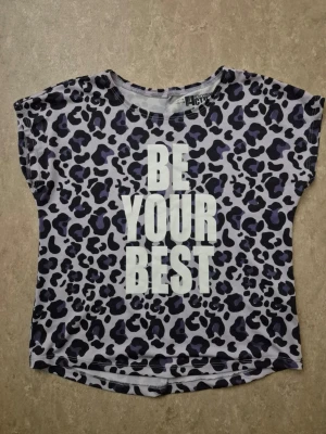 T-shirt - Cool t-shirt från mywearActive med leopardmönster i svart och lila på ljusgrå bakgrund. Stort vitt tryck med texten 'BE YOUR BEST' på framsidan. Kortärmad och tillverkad i mjuk polyester, perfekt för dig som vill sticka ut.