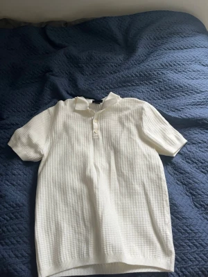 Vit piké från H&M med struktur - Säljer en vit piké från H&M i regular fit med korta ärmar och krage. Toppen har en snygg strukturerad yta och knäppning framtill med två knappar. Perfekt för en clean och fräsch look.