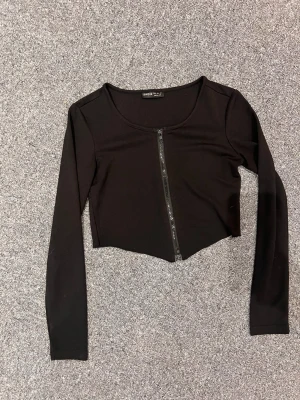 Svart croppad topp från SHEIN - Snygg svart croppad topp från SHEIN med lång ärm och dragkedja framtill. Enkel och stilren design som passar till många olika looks. Tillverkad i mjukt och stretchigt material för en bekväm passform.