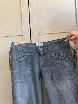 Blå bootcut jeans från Lee - Säljer ett par ljusblå bootcut jeans från Lee med raka ben och coola fickdetaljer framtill. Jeansen har låg midja och klassisk knappgylf. Detta är ett par jeans som gör hela outfiten! 