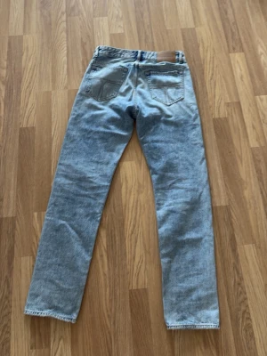 Ljusblå raka jeans Tiger of Sweden - Säljer ett par ljusblå jeans från Tiger of Sweden med rak passform och klassisk femficksdesign. Jeansen har en vintagekänsla och är tillverkade i slitstarkt denimtyg. Perfekta för en avslappnad och trendig look.