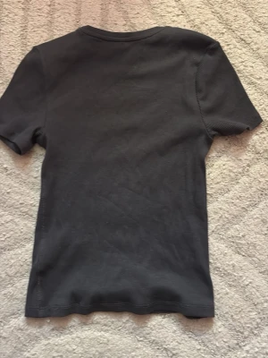 Svart ribbad t-shirt från HM  - En enkel grå t-shirt från HM med ribbad struktur. Modellen har rund halsringning och korta ärmar. Perfekt basplagg som funkar till det mesta och är tillverkad i mjuk bomull. Pris kan diskuteras 💓Har använt tröjan cirka 2 gånger så den är typ helt ny 💓