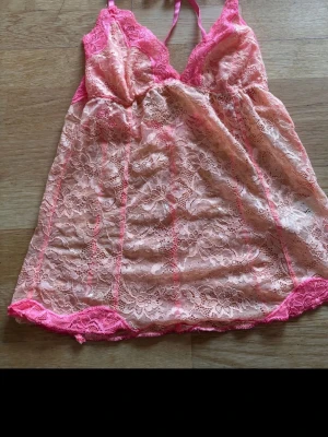 Vintage Rosa top - Säljer ett sött nattlinne i ljusrosa spets med starkrosa spetsdetaljer. Nattlinnet har tunna axelband och v-ringning, samt blommigt spetsmönster över hela plagget. Perfekt för dig som gillar romantisk och feminin stil.