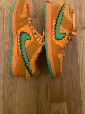 Nike SB Dunk Low Grateful Dead Orange - Unika sneakers från Nike SB Dunk Low Grateful Dead i orange mocka och fluffigt tyg. Skon har gröna detaljer, inklusive sula och den ikoniska Swoosh-loggan med svart taggig kant. Skosnören i orange och cool kontrast mellan material och färger. Perfekt för dig som vill sticka ut.