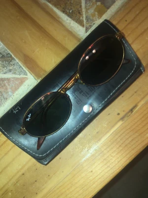 RayBan - Side Street. Äkta riktigt fina solglasögon. - Säljer ett par ikoniska Ray-Ban solglasögon med rund form och tunna guldfärgade metallbågar. Glasen är mörka och klassiskt svarta. Kommer med original Ray-Ban fodral. Perfekta för dig som vill ha en tidlös och trendig look.. Dessa är äkta o nypris är på 1400kr. Kvitto finns. Säljer för 500 pris går diskutera vid snabb affär.