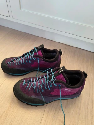 Haglöfs Roc Icon Q Gt | Friluftsskor stl. 40 - Säljer ett par lila vandrings- hikingskor med Gore-Tex membran och turkosa snören. Skorna har slitstark Vibram-sula, tålig gummiförstärkning runt tån och meshpaneler för bra ventilation. Perfekta för utomhusaktiviteter och äventyr. Nyskick, säljes pga fel storlek.