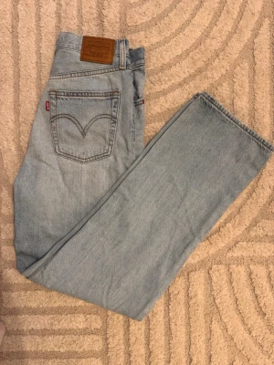 Ljusblå Levi's jeans raka ben - Säljer ett par klassiska ljusblå Levi's jeans med raka ben och hög midja. Jeansen har den ikoniska läderlappen bak i midjan och Levi's röda etikett på bakfickan. Perfekta till alla tillfällen och superenkla att styla.