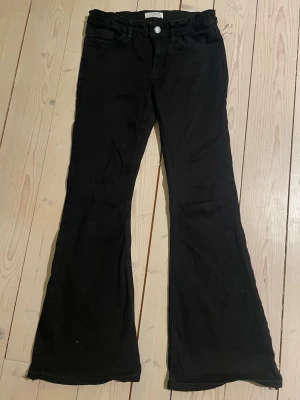 Svarta bootcut jeans - Snygga svarta bootcut jeans från Lindex med klassisk femficksmodell och knappgylf. Jeansen har utsvängda ben och är tillverkade i ett stretchigt denimtyg som sitter bekvämt. Dom är uppsprättad där nere, därför passar de någon som är mellan 152-155