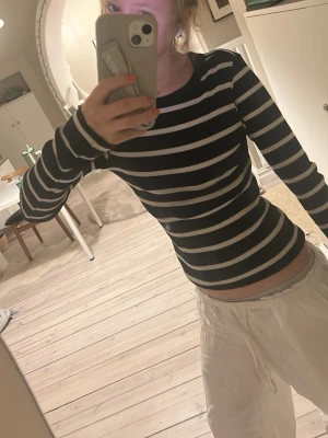 Svart och vit randig långärmad topp - En svart och vit randig långärmad topp med tight passform och rund halsringning. Perfekt för dig som gillar en enkel men snygg stil. Materialet ser ut att vara bomull eller polyester och toppen är ribbad för extra komfort.