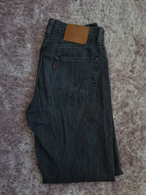 Levi's 555 svarta raka jeans W29 L32 - Säljer ett par svarta Levi's 555 jeans med rak passform. Jeansen har en snygg tvättad look, läderpatch bak i midjan och röd Levi's-tagg på bakfickan. Perfekta för en avslappnad och stilren outfit.