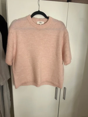 Ljusrosa stickad tröja Gina Tricot - Mysig ljusrosa stickad tröja från Gina Tricot i ullblandning. Tröjan har korta ärmar, rund halsringning och en boxig, avslappnad passform. Perfekt för lager på lager och en söt detalj i garderoben.