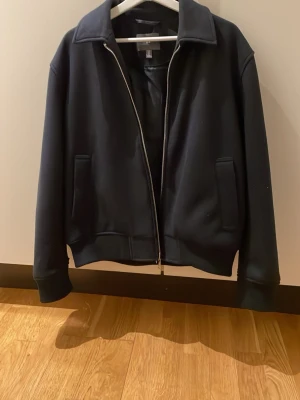 Svart zip-jacka från H&M - Stilren svart jacka från H&M med rak passform och dragkedja framtill. Jackan har två fickor på sidorna och en klassisk krage. Perfekt för dig som gillar en enkel och clean look. Materialet känns mjukt och bekvämt.