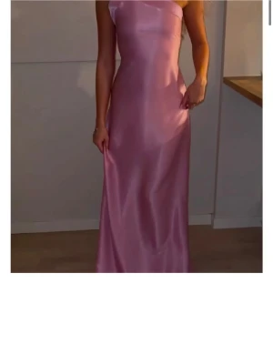 Rosa långklänning i satin - Klänning som är köpt från Vinted och enligt beskrivning är använd 1 gång på baldagen. 💗💗Snygg rosa långklänning i satin med oneshoulder och öppen rygg. Klänningen har en elegant slät yta och ett band som knyts i ryggen för extra detalj. 