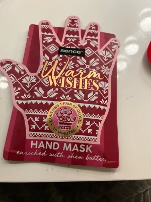 Sence Warm Wishes Hand Mask - Handmask från Sence i röd och vit förpackning formad som en vante. Innehåller ett par handmaskhandskar berikade med sheasmör. Masken är vegansk och används i 20 minuter för att återfukta och vårda händerna.