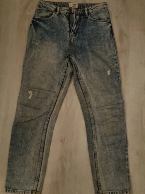 Blå tvättade jeans från Denim Collection - Säljer ett par blå tvättade jeans från Denim Collection med raka ben och slitna detaljer på framsidan. Jeansen har klassisk femficksmodell, bälteshällor och råa kanter vid benslut. Perfekta för en avslappnad och trendig look.