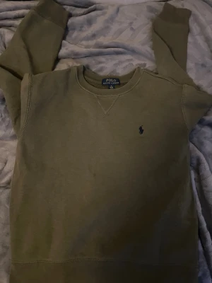 Olivgrön sweatshirt från Polo Ralph Lauren - Säljer en olivgrön sweatshirt från Polo Ralph Lauren med klassisk rund halsringning och diskret broderad logga på bröstet. Tröjan har ribbade muddar vid ärmslut och nederkant. Perfekt för en avslappnad och stilren look. Tröjan är i superbra skick endast provad!