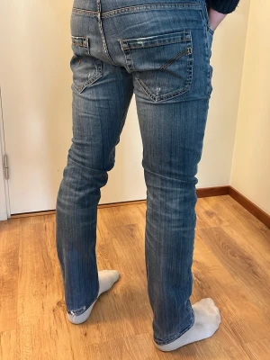 Dondup jeans - Säljer ett par blå jeans med raka ben och diskreta slitningar. Jeansen har klassiska fem fickor, dragkedja och knapp i midjan. Materialet är denim med en snygg tvättad look och kontrastsömmar. Perfekta för en avslappnad och trendig stil.